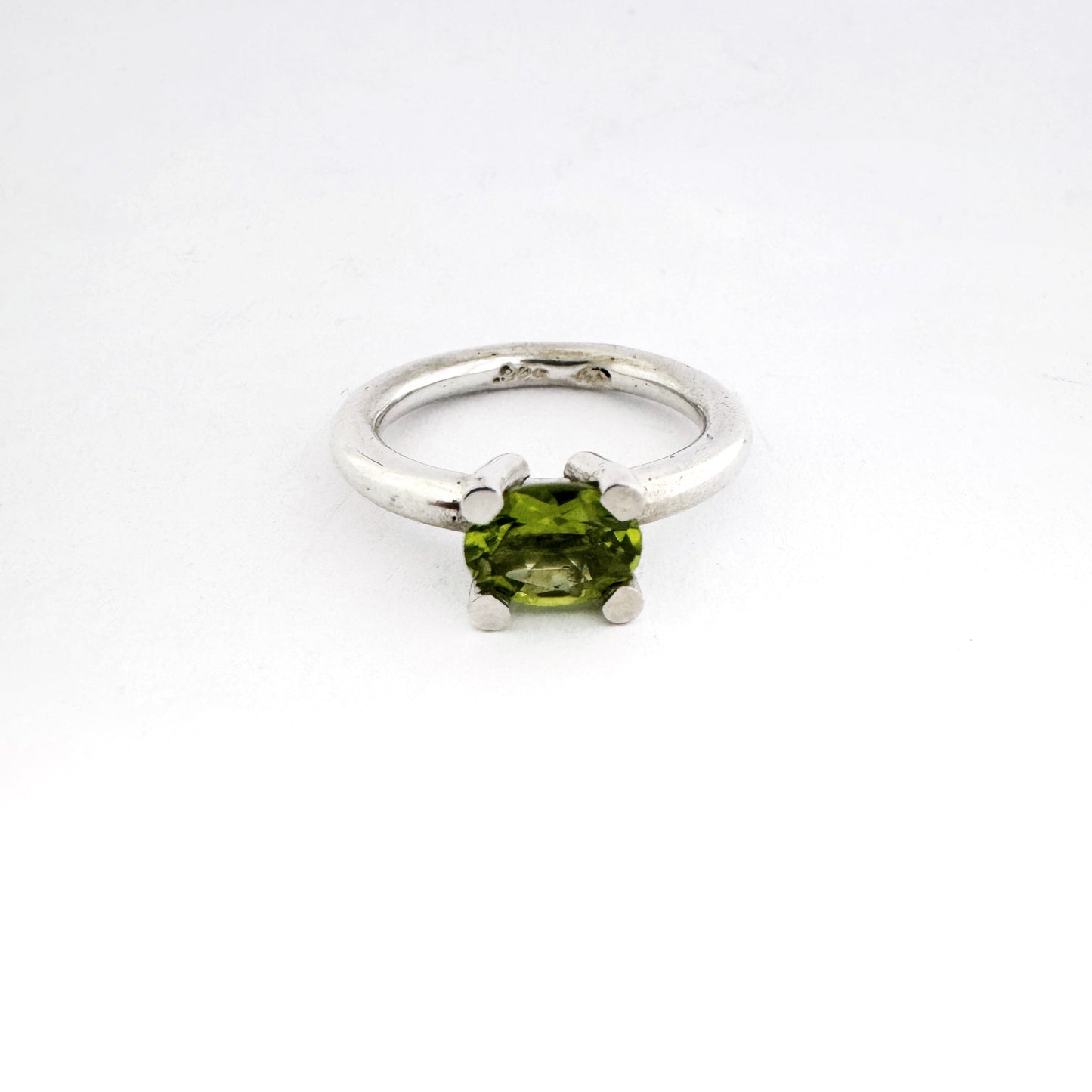 A silver ring featuring a green peridot gemstone in a four-prong setting, photographed on a seamless white background.