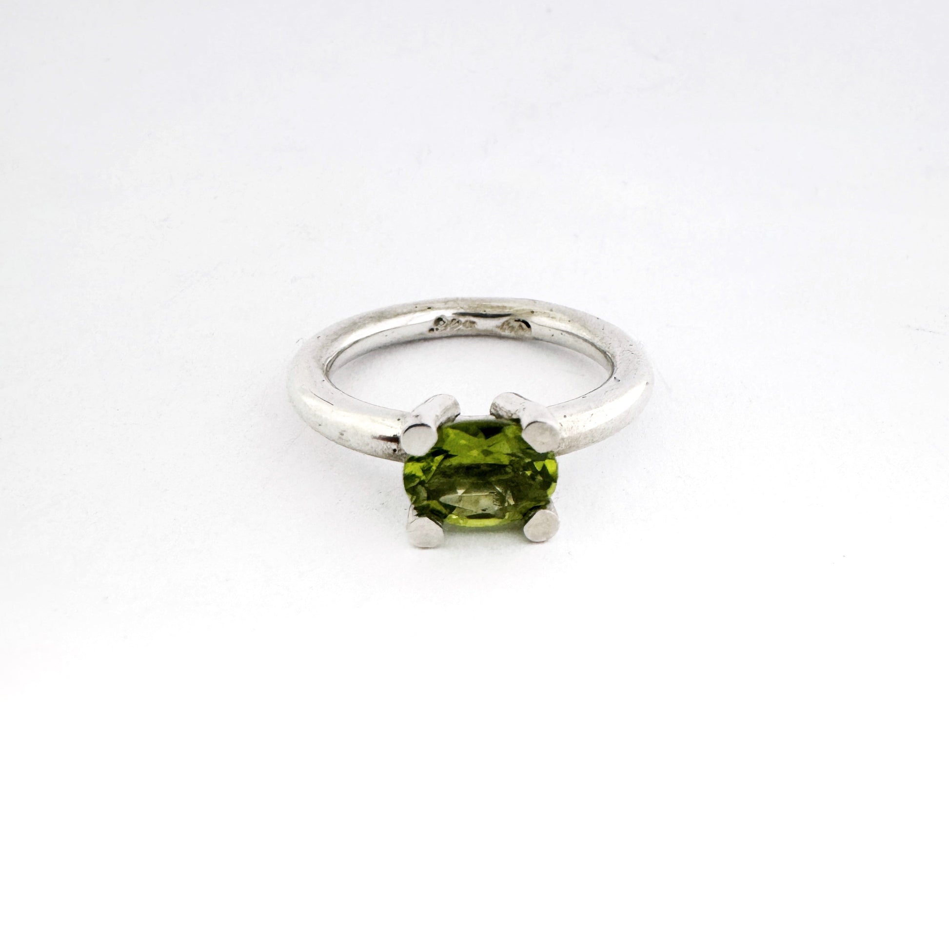 A silver ring featuring a green peridot gemstone in a four-prong setting, photographed on a seamless white background.