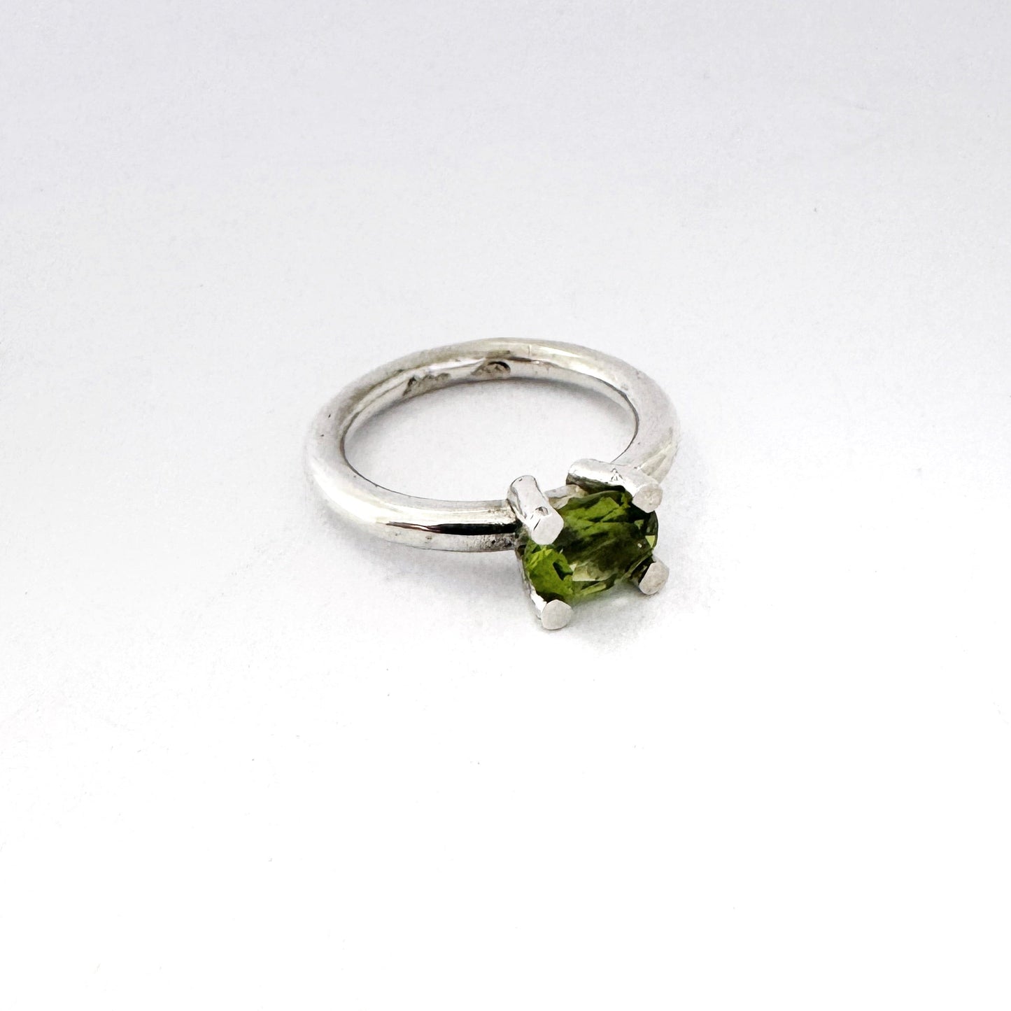 A sterling silver ring featuring a single oval-cut green gemstone in a prong setting, displayed on a clean white background.