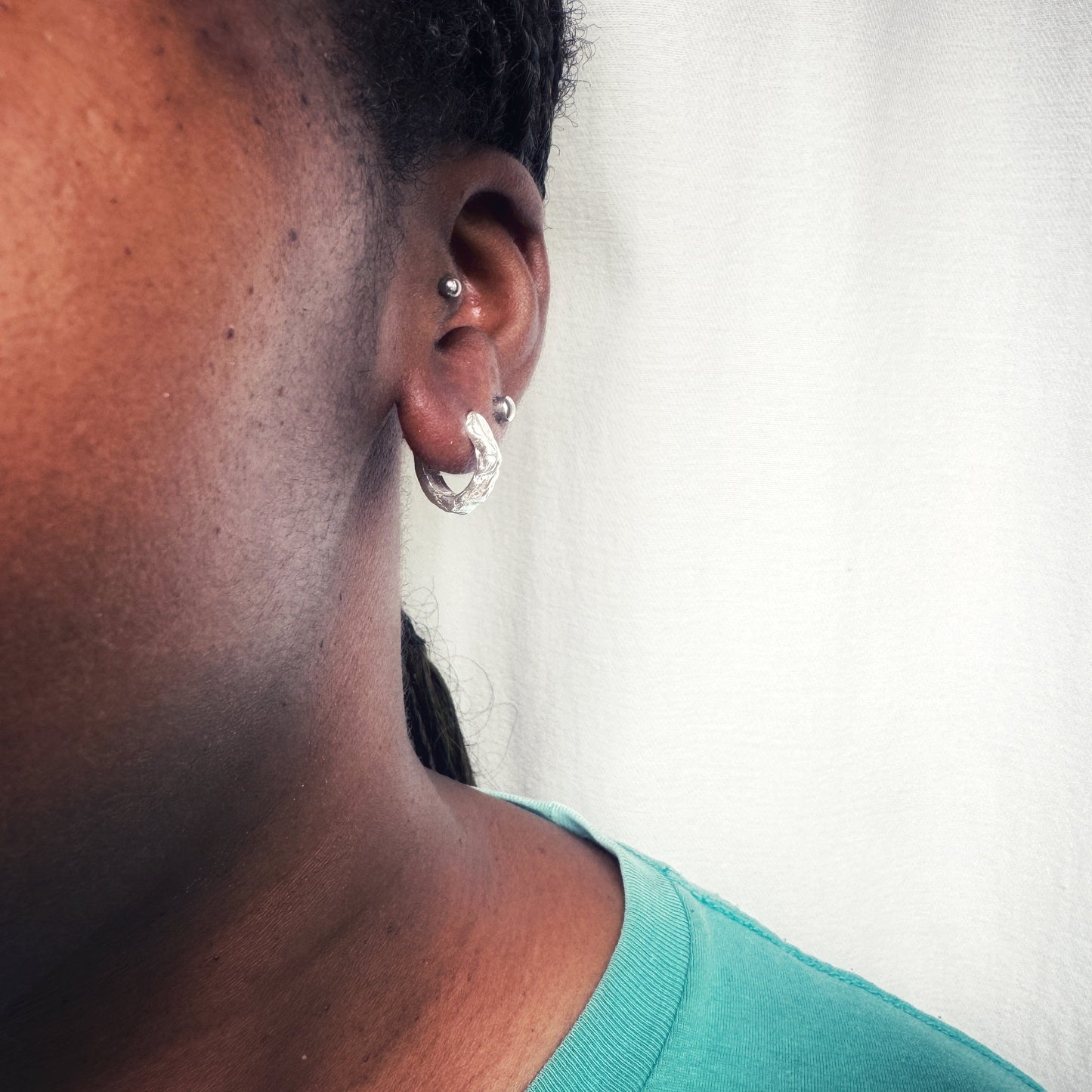 Close-up of an ear with an organic silver earring against a neutral background